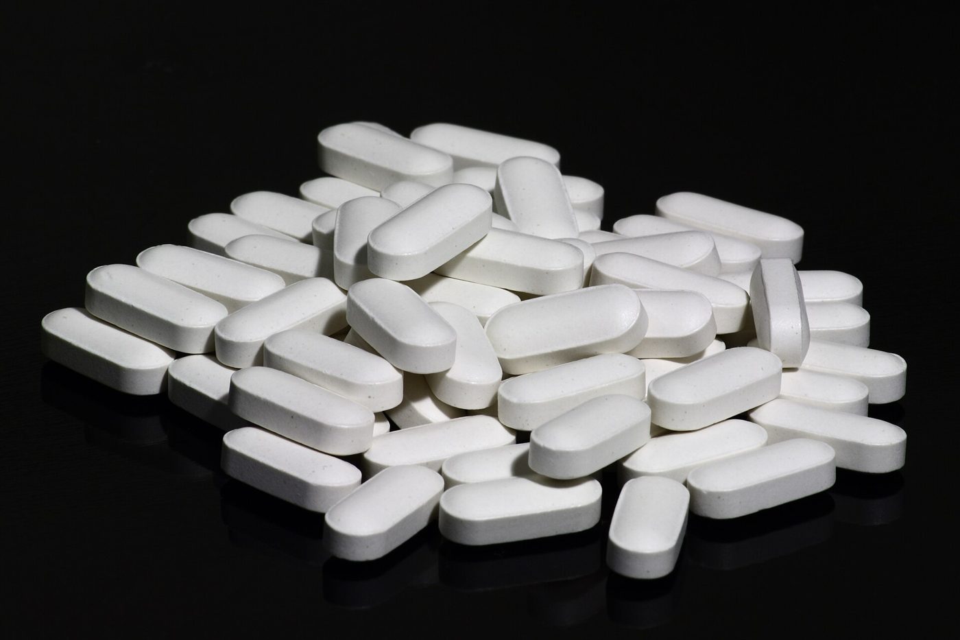 En hög vita avlånga tabletter med kalcium och D-vitamin mot svart bakgrund