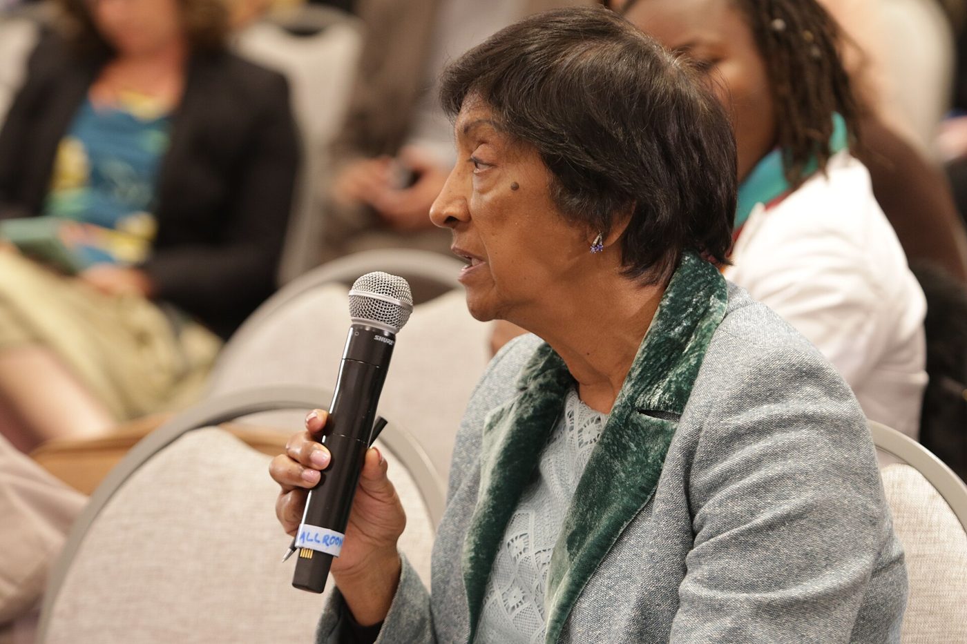 Navi Pillay, i grå kavaj med grön sammetskrage, talar i en mikrofon under ett seminarium